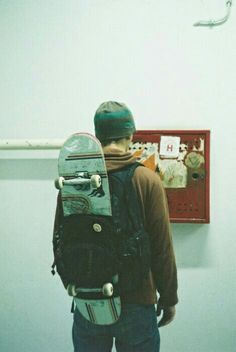 a man with a skateboard in his back pack standing next to a wall hanging on the wall