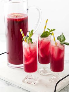 three glasses filled with red liquid and mint garnish on a white marble tray