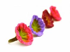 three different colored flowers sitting on top of a white surface with one flower in the middle