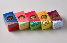 six colorful boxes with cookies in them on a white surface, lined up against each other