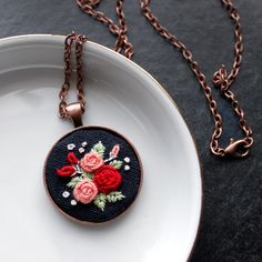 a white plate topped with a necklace and a red rose pendant on a black surface