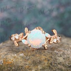 an opal and diamond ring sitting on top of a rock with leaves around it