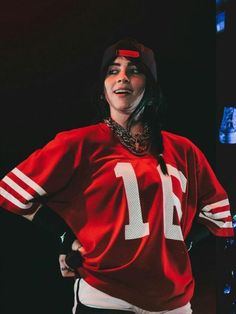 a woman wearing a red jersey with white letters on the front and side, standing in front of a black background