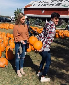 two people standing next to each other with pumpkins on the ground in front of them