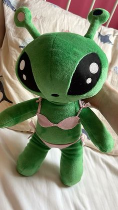 a green stuffed toy sitting on top of a bed