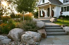 a house is shown with large rocks in the foreground and flowers on the front lawn