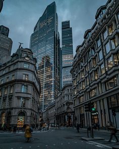 a city street with tall buildings in the background at dusk, and people walking on the sidewalk