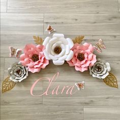 the name clara is surrounded by paper flowers and butterflies on a wooden floor with wood planks