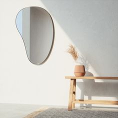 a wooden bench sitting next to a white wall with a round mirror on the wall