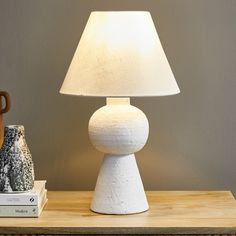 a white lamp sitting on top of a wooden table next to a book and vase