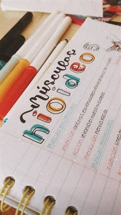 an open notebook with writing on it next to markers and pencils in front of them