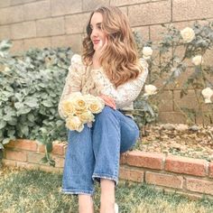 a woman sitting on a brick wall holding a bouquet of flowers in her hand and smiling