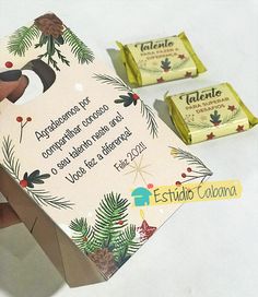 someone is holding two chocolate bars in front of each other on a white table with pine cones and evergreen leaves