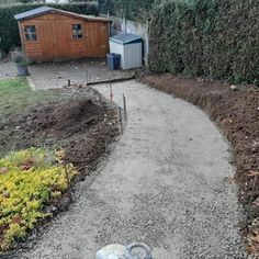 a dog laying on the ground in front of a fence and yard with a shed behind it