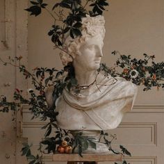 a white marble bust sitting on top of a table covered in flowers and foliage next to a wall