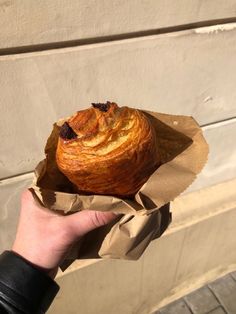 a hand holding a pastry wrapped in brown paper