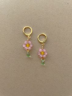 two small pink and yellow flowers are hanging from gold hoop earrings