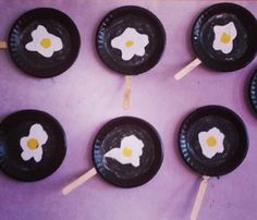 six black plates with white flowers on them and popsicle sticks sticking out of them