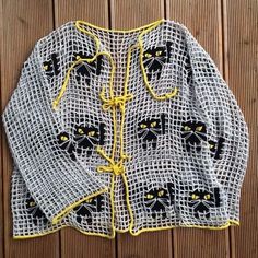 a knitted jacket with yellow and black cats on the front, sitting on a wooden surface