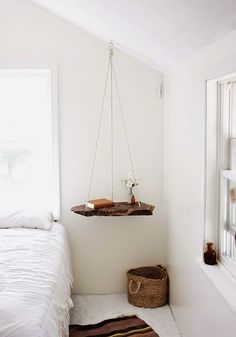 a bedroom with white walls and flooring has a hanging shelf above the headboard