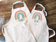 two personalized aprons with rainbow designs on them sitting next to each other in front of a wooden table