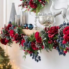 a christmas wreath with red flowers and greenery hanging on the wall next to a fireplace