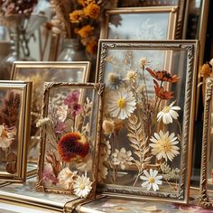 four framed pictures with flowers in them sitting on a table next to other frames and vases