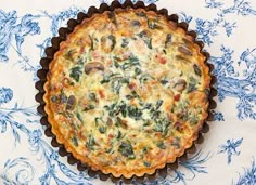 a quiche with spinach and cheese in a pie pan on a blue floral tablecloth