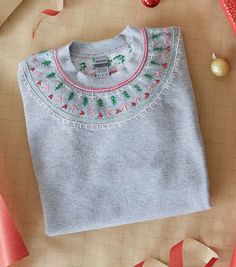 a gray sweater with christmas decorations and ribbon on the table next to it is an ornament