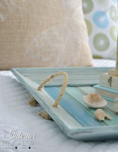 a tray with books and seashells sitting on top of a bed next to a pillow