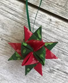 a red and green origami star hanging from a string on a wooden surface