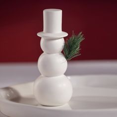 a white snowman sitting on top of a plate with a pine tree in it