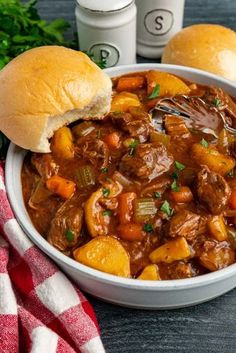 a bowl filled with beef and potatoes next to two rolls