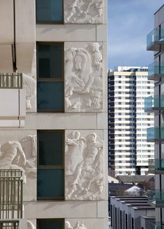 a tall white building with windows and statues on it's side in front of other buildings