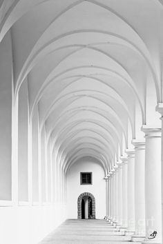 black and white photograph of an empty hallway with arches on both sides, looking towards the door