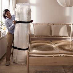 a woman standing next to a bed with a mattress on it