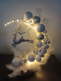 a white and silver christmas decoration with lights on the top, surrounded by balls and feathers