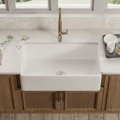 a white kitchen sink sitting on top of a counter next to wooden cabinets and windows