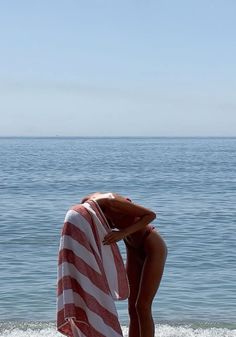 a woman standing on the beach with a towel wrapped around her head looking out at the ocean