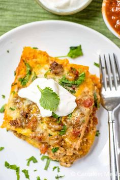 a white plate topped with lasagna casserole covered in sour cream and garnished with cilantro