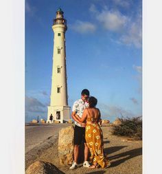 a man and woman standing in front of a light house with the ocean in the background