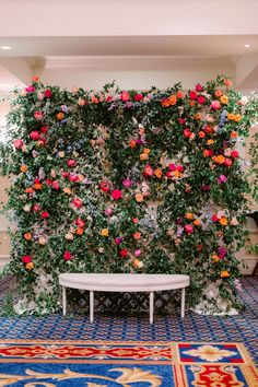 a white bench sitting in front of a wall covered with pink and orange flowers on it's side