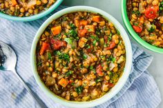 three bowls filled with beans and vegetables on top of a blue towel next to spoons