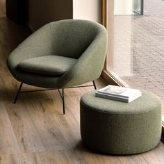 a green chair sitting next to a window with a book on top of the ottoman