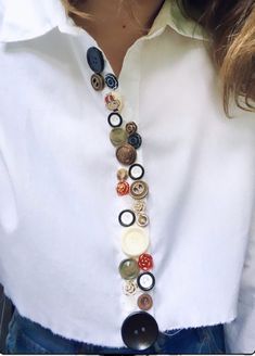 a woman wearing a white shirt with buttons attached to her neck and holding onto a button necklace