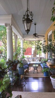 a porch with potted plants on the side and an old fashioned lamp hanging from the ceiling