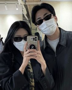 a man and woman wearing face masks taking a selfie with their cell phone in front of them