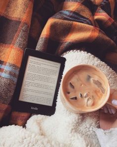 someone is reading a book and holding a cup of coffee while laying on a blanket