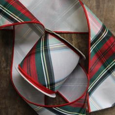 a red, green and white plaid bow tie on a wooden table with other ties