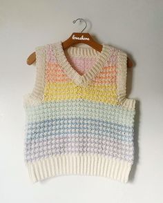 a white sweater with multicolored stripes is hanging on a wooden hanger against a white wall